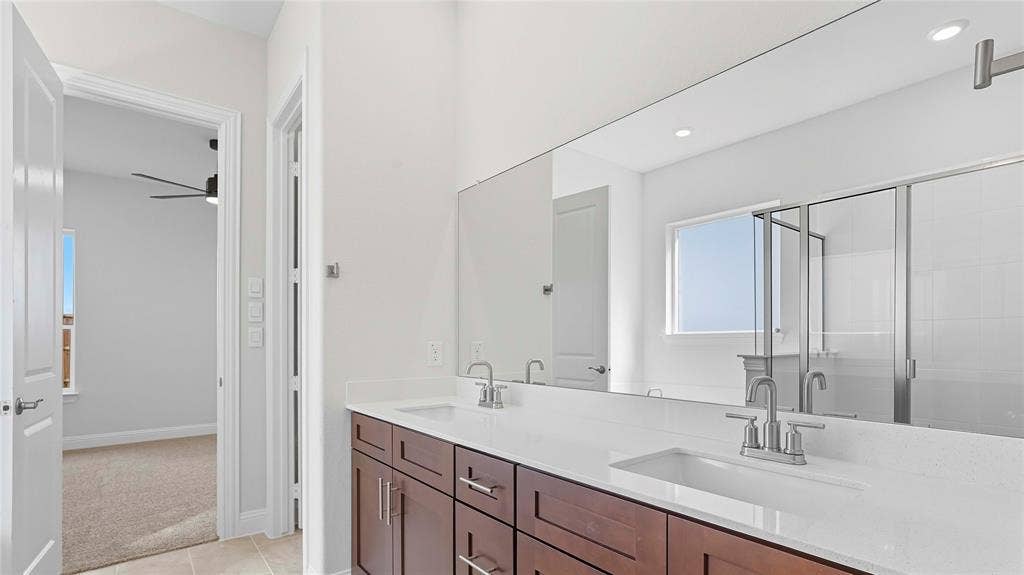 Dual-sink vanity with white stone-finish countertop, dark wood-finish cabinetry, full-width mirror, and walk-in shower with glass enclosure
