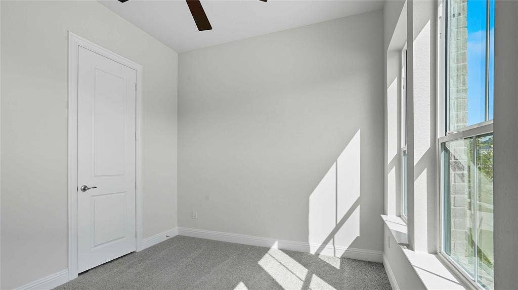 Interior room featuring neutral-toned carpeting, a ceiling fan, a multi-panel interior door with brushed metallic hardware, and tall windows with brick exterior detailing