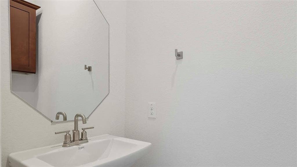 Wall-mounted wood-finish cabinet, geometric mirror, white pedestal sink, and brushed-nickel dual-handle faucet