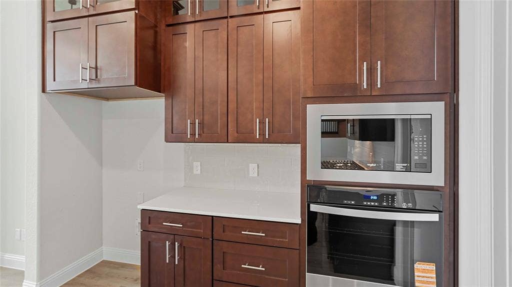 Dark wood-finish cabinetry featuring shaker-style doors, stone-surface countertops, and stainless steel built-in microwave and oven combination