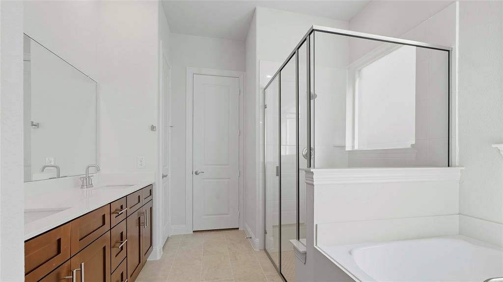 Dual-sink vanity with light-toned solid surface countertop, glass-enclosed shower, soaking tub, and tile flooring