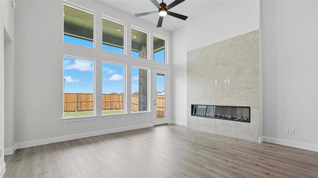 High-ceiling room featuring large floor-to-ceiling windows, wood-finish flooring, a full-height tile fireplace surround with a linear insert, and a ceiling fan