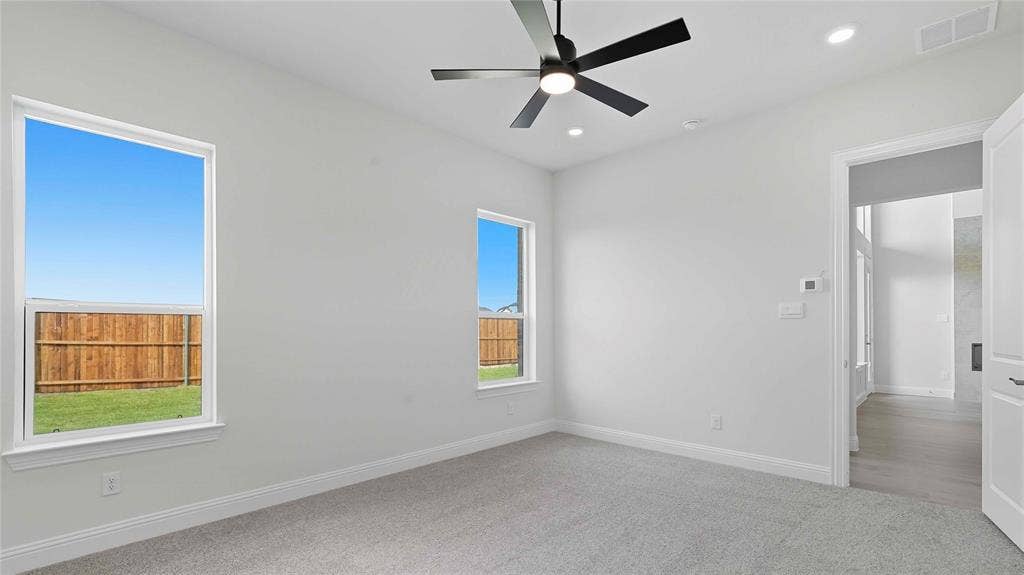 Neutral-toned interior featuring plush carpeting, a modern matte black ceiling fan, recessed lighting, and large windows providing natural light