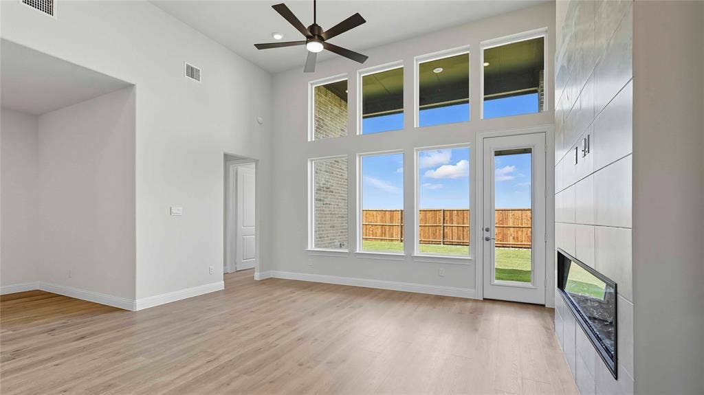 High-ceiling living area featuring wood-finish flooring, a wall-mounted fireplace with large-format tile surround, multiple rows of oversized windows, and a dedicated ceiling fan