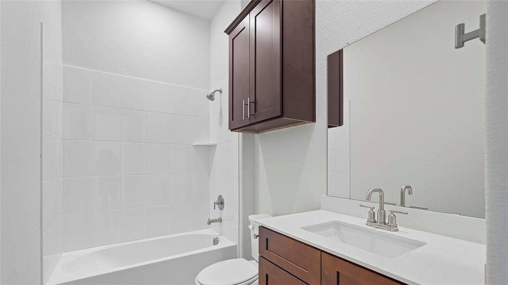 Bathroom featuring a white vanity with a composite countertop, dark wood-finish cabinetry, a large frameless mirror, and a tile-surround tub-shower combination