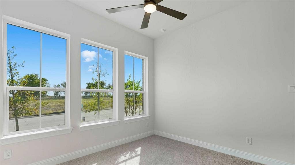 Room featuring neutral-toned carpeting, three large multi-pane windows, and a matte black ceiling fan with integrated lighting