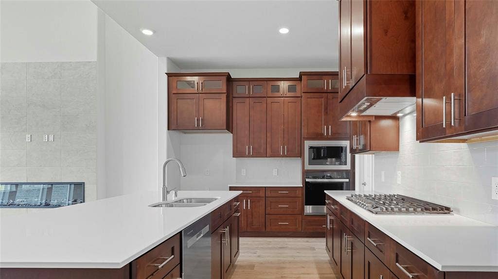 Kitchen featuring custom stained-wood cabinetry, white stone countertops, built-in stainless steel double wall ovens, a gas cooktop, and wood-finish flooring