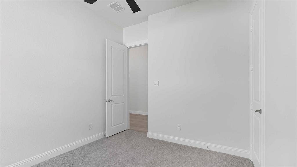 Interior space featuring neutral wall tones, plush wall-to-wall carpeting, and a ceiling-mounted matte black fan, accented by solid-core paneled doors with brushed nickel hardware