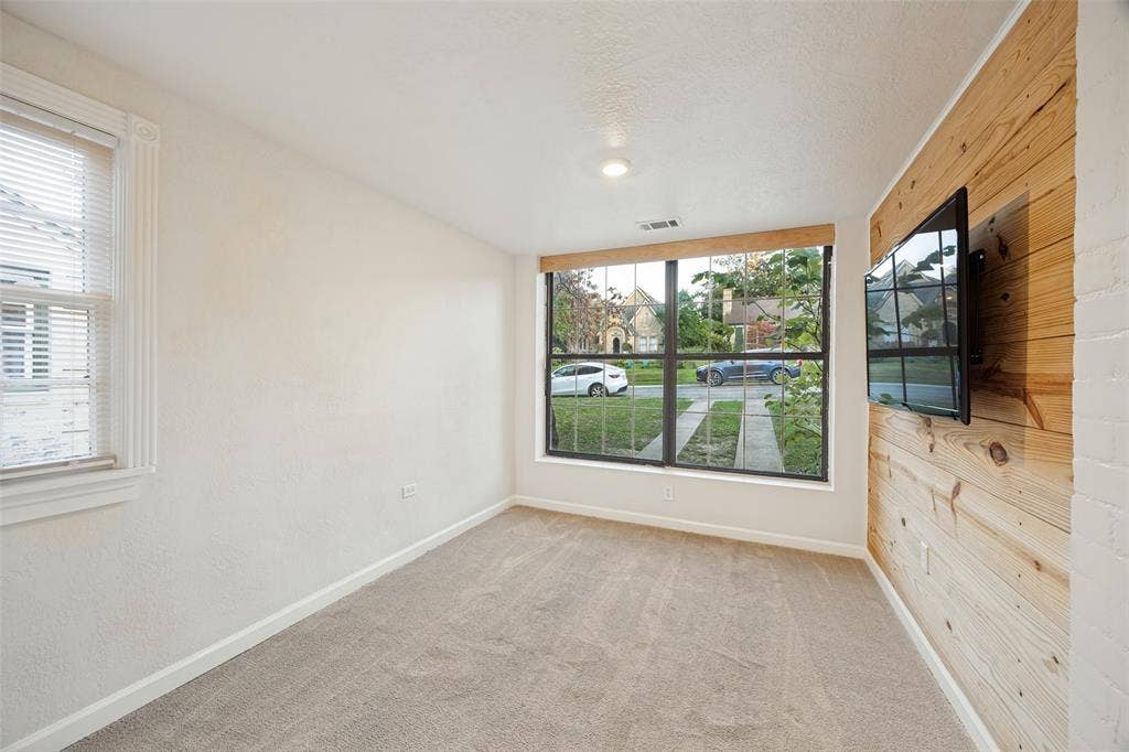 7011 Hammond Avenue, Dallas, TX 75223 Room featuring a natural wood-plank accent wall, large picture window with dark framing, neutral wall-to-wall carpeting, and recessed lighting