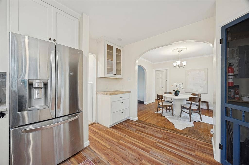 7011 Hammond Avenue, Dallas, TX 75223 Kitchen featuring white cabinetry with glass-front display uppers, wood-finish flooring, and stainless steel refrigerator