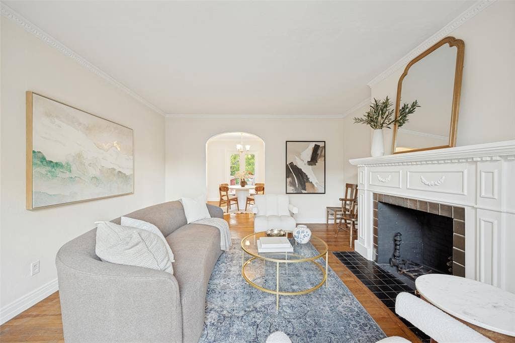 7011 Hammond Avenue, Dallas, TX 75223 Living area featuring wood-finish flooring, a traditional white fireplace mantel, black tile hearth, and arched architectural detailing