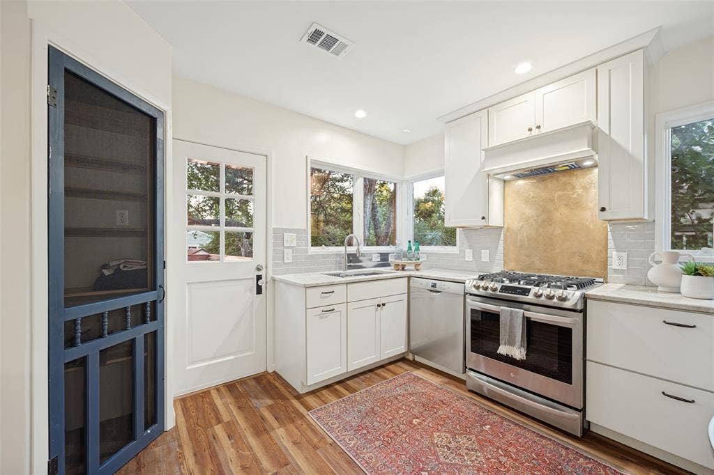7011 Hammond Avenue, Dallas, TX 75223 Kitchen featuring shaker-style cabinetry, stainless steel appliances, stone-finish countertops, subway tile backsplash, and wood-finish flooring