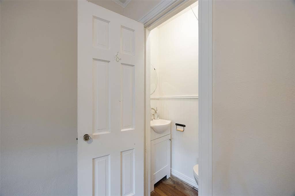 7011 Hammond Avenue, Dallas, TX 75223 Six-panel interior door with brushed metal hardware opening to a compact vanity featuring a wall-mounted sink, wood-finish flooring, and horizontal wall wainscoting