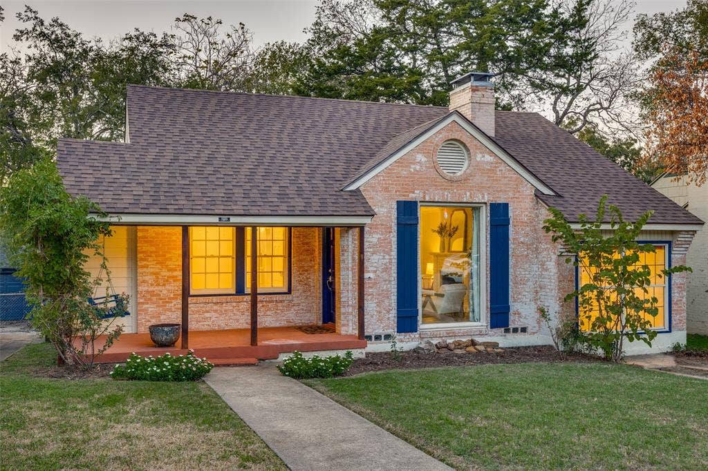 7011 Hammond Avenue, Dallas, TX 75223 Brick exterior featuring a covered front porch, asphalt shingle roofing, decorative window shutters, and a circular gable vent