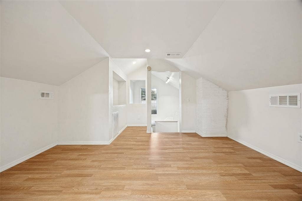 7011 Hammond Avenue, Dallas, TX 75223 Vaulted ceilings with recessed lighting, wood-finish flooring, built-in shelving, and a painted brick accent wall