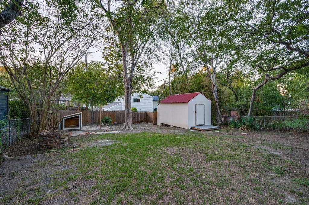7011 Hammond Avenue, Dallas, TX 75223 Spacious backyard featuring mature trees, a detached storage structure with a metal roof, and perimeter fencing