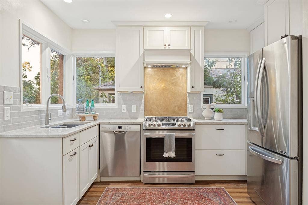 7011 Hammond Avenue, Dallas, TX 75223 Kitchen featuring white cabinetry, stainless steel appliances, light-toned countertops, subway tile backsplash, and a metallic range backsplash