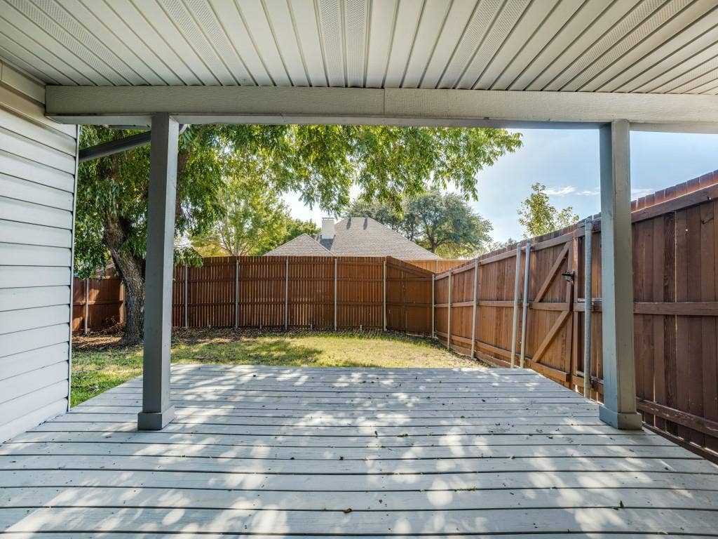900 Lexington Drive, Plano, TX 75075 Covered patio with wood-finish decking and structural pillars, encompassing a fenced backyard featuring a grassy lawn and mature trees