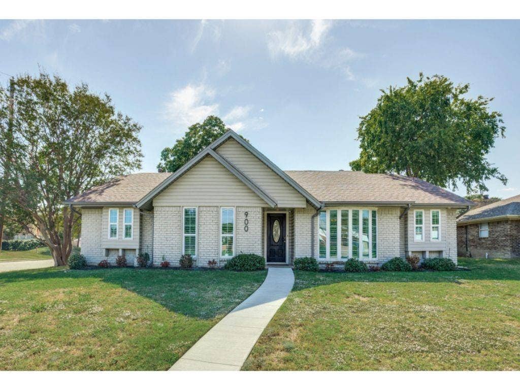 900 Lexington Drive, Plano, TX 75075 Single-story residence featuring a light-toned brick and horizontal siding exterior, a front-facing gable roof, a centered entrance with an oval-glass door, and a multi-pane bay window