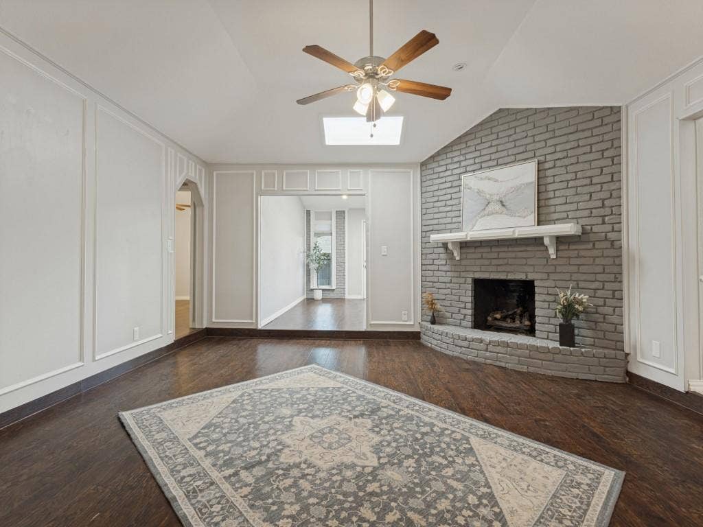 900 Lexington Drive, Plano, TX 75075 Vaulted ceiling with a skylight, wood-finish flooring, floor-to-ceiling wainscoting, and a painted brick fireplace with a decorative mantel
