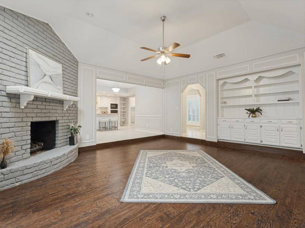 900 Lexington Drive, Plano, TX 75075 Vaulted ceilings, wood-finish flooring, painted brick fireplace with a decorative mantel, and built-in floor-to-ceiling cabinetry with millwork detailing