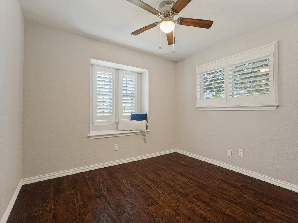 900 Lexington Drive, Plano, TX 75075 Neutral-toned room featuring dark wood-finish flooring, a ceiling fan with integrated lighting, plantation shutters, and a built-in window seat