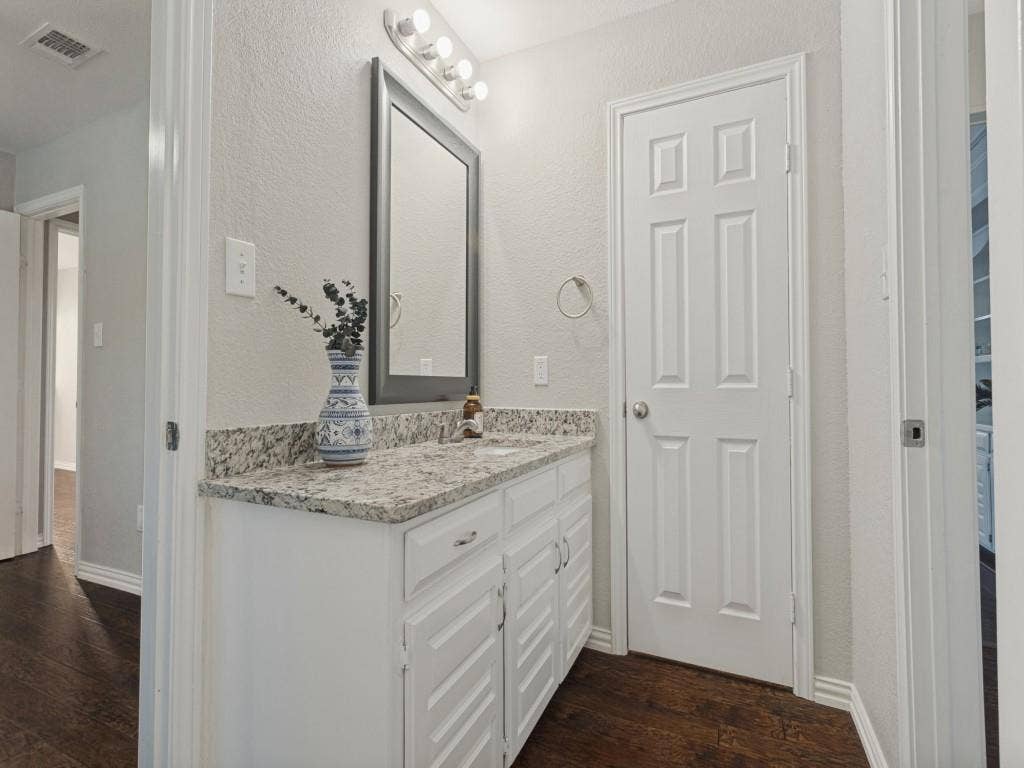 900 Lexington Drive, Plano, TX 75075 White vanity cabinet with a stone countertop, integrated sink, framed mirror, and multi-bulb vanity light fixture