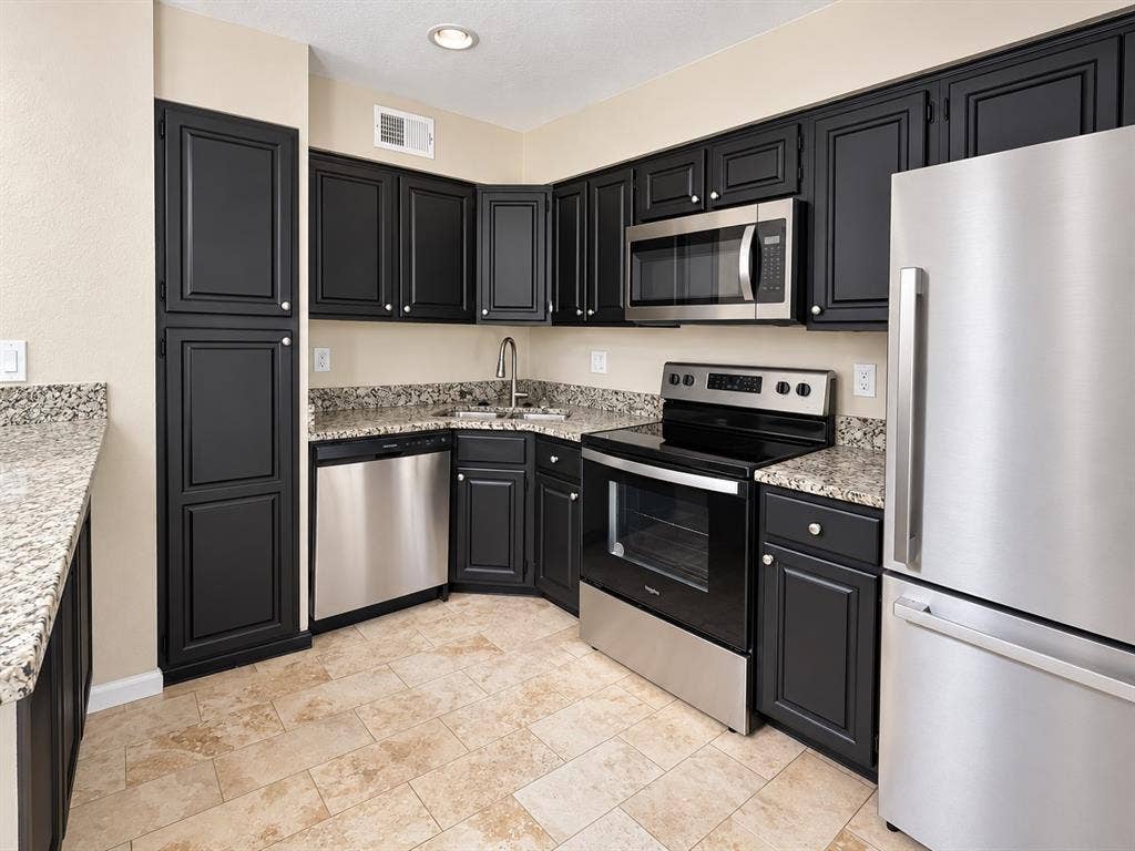7525 Holly Hill Drive, #20, Dallas, TX 75231 Kitchen featuring black shaker-style cabinetry, stone-finish countertops, stainless steel appliances, and tile flooring