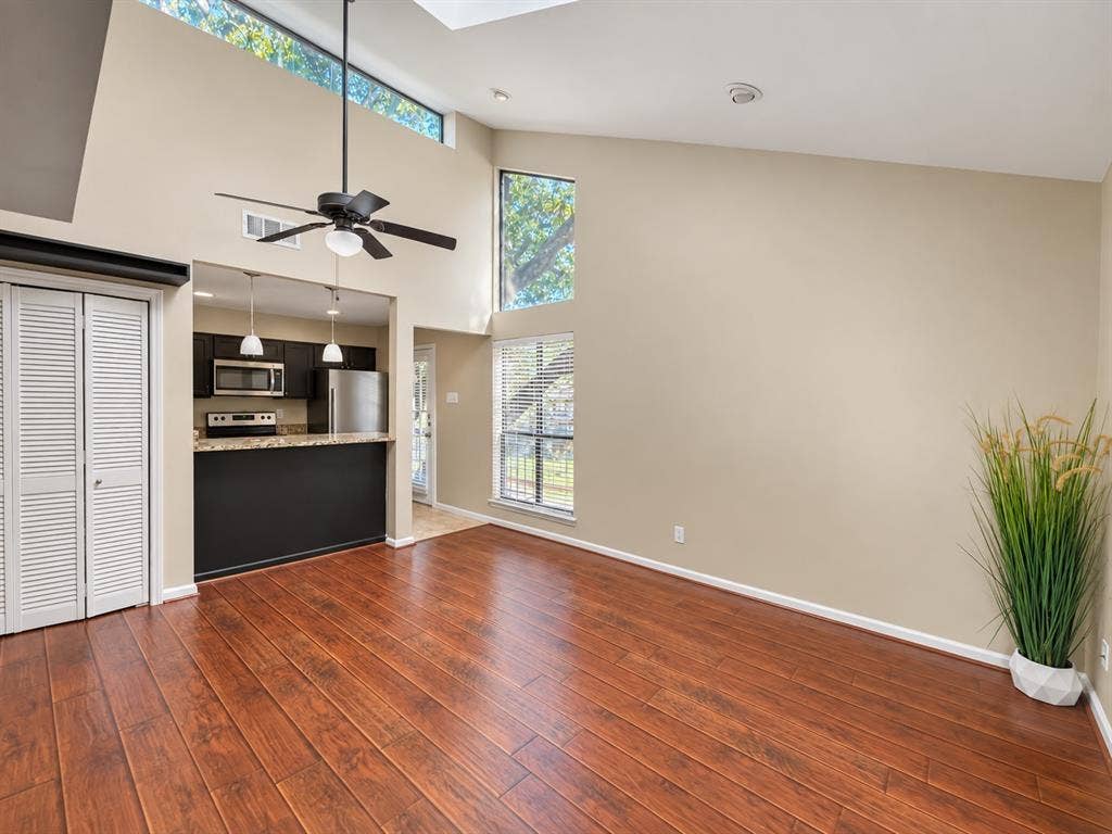 7525 Holly Hill Drive, #20, Dallas, TX 75231 Vaulted ceiling with clerestory windows, wood-finish flooring, and recessed kitchen area featuring stainless steel appliances and stone-surface breakfast bar