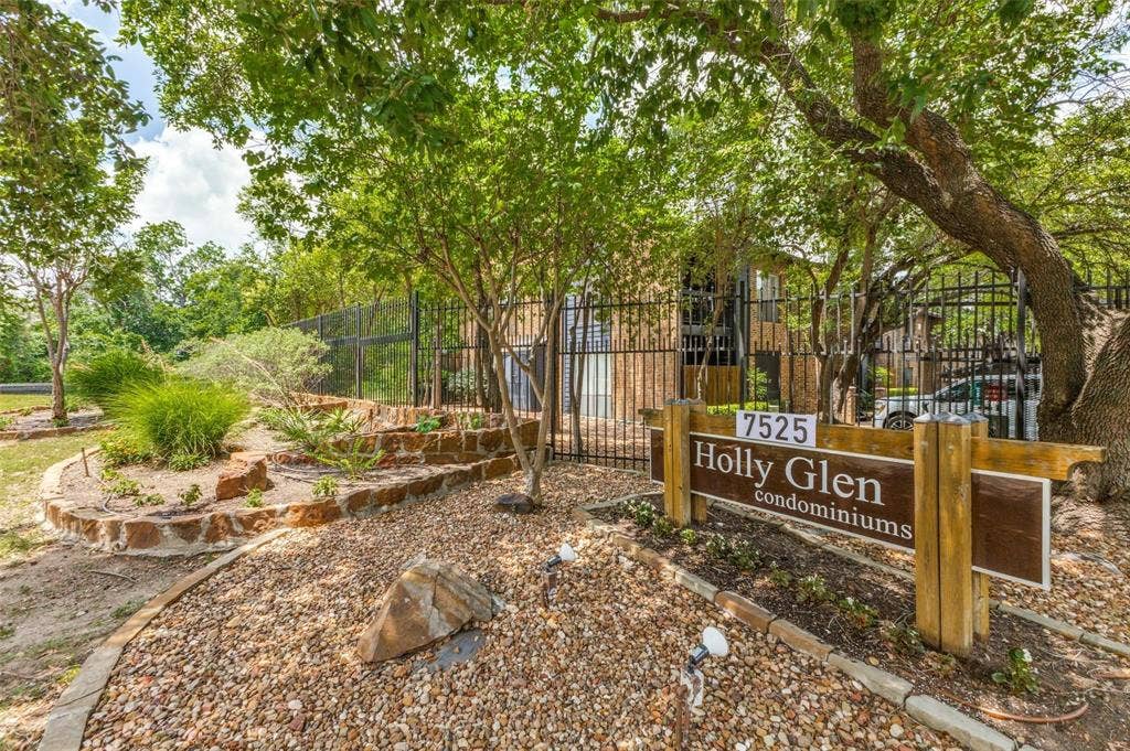 7525 Holly Hill Drive, #20, Dallas, TX 75231 Exterior signage featuring wood-post construction, stone-retaining walls, gravel landscaping, and mature trees