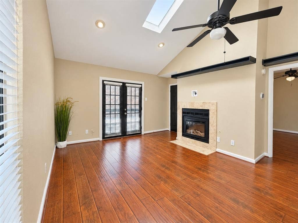 7525 Holly Hill Drive, #20, Dallas, TX 75231 Vaulted ceiling featuring a skylight, wood-finish flooring, fireplace with a tiled surround, and black-framed French doors
