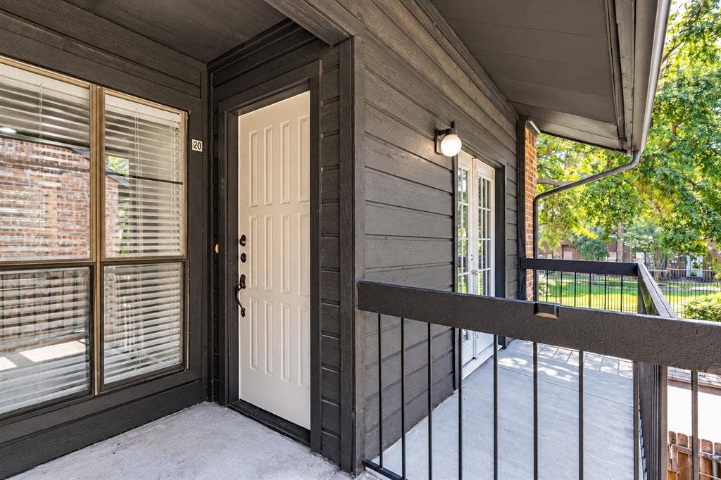 7525 Holly Hill Drive, #20, Dallas, TX 75231 Covered balcony featuring dark horizontal wood siding, a paneled door, black metal railings, and an exterior wall-mounted light fixture