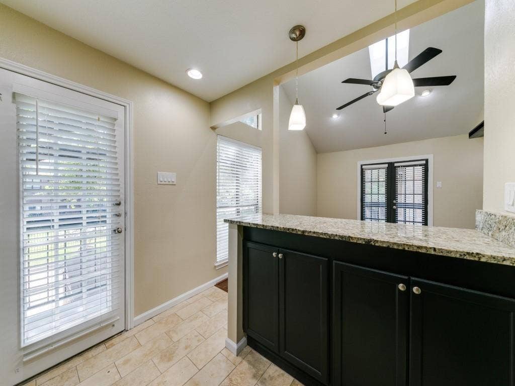 7525 Holly Hill Drive, #20, Dallas, TX 75231 Kitchen features dark-finish cabinetry, stone-patterned countertops, tile flooring, dual pendant lighting, and a vaulted ceiling with a mounted ceiling fan