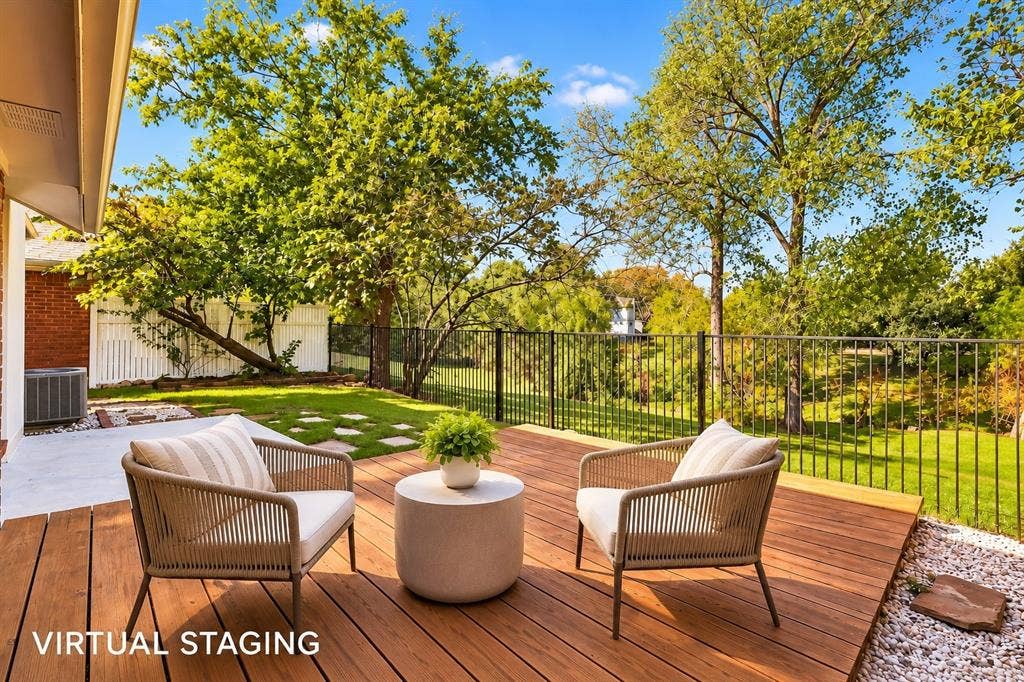 6821 Douglas Creek, Plano, TX 75023 Rear wood-plank deck featuring a black metal perimeter fence, concrete patio area, and mature perimeter trees