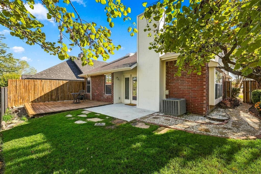 6821 Douglas Creek, Plano, TX 75023 Backyard featuring brick exterior walls, a wood deck, a concrete patio, a central chimney, and stone-accented landscape pathways