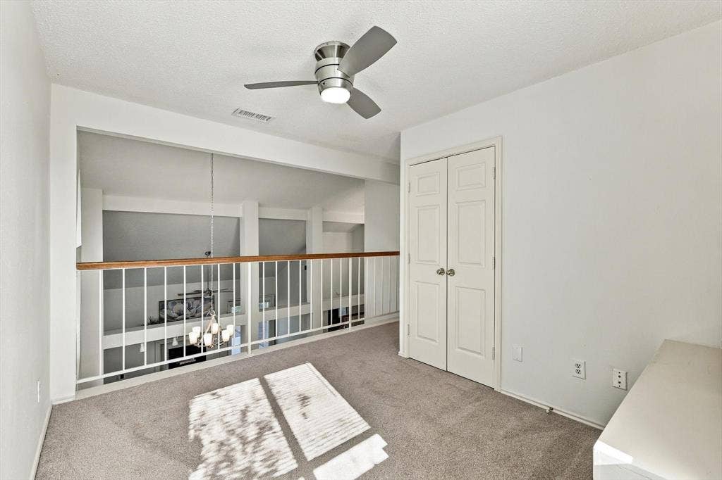 6821 Douglas Creek, Plano, TX 75023 Neutral-toned carpet, metallic ceiling fan with integrated lighting, and white bi-fold closet doors, featuring a white metal railing with a wood-finish cap