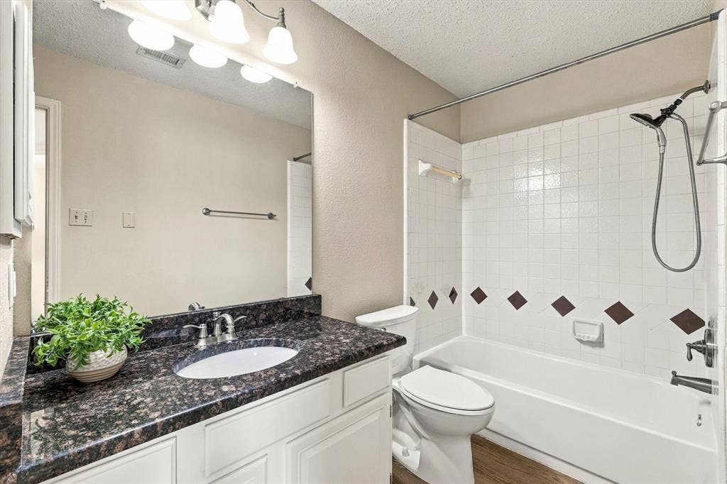 6821 Douglas Creek, Plano, TX 75023 Bathroom featuring a stone-look countertop, undermount sink, multi-bulb vanity light, and a tiled shower-tub combination with an adjustable handheld showerhead