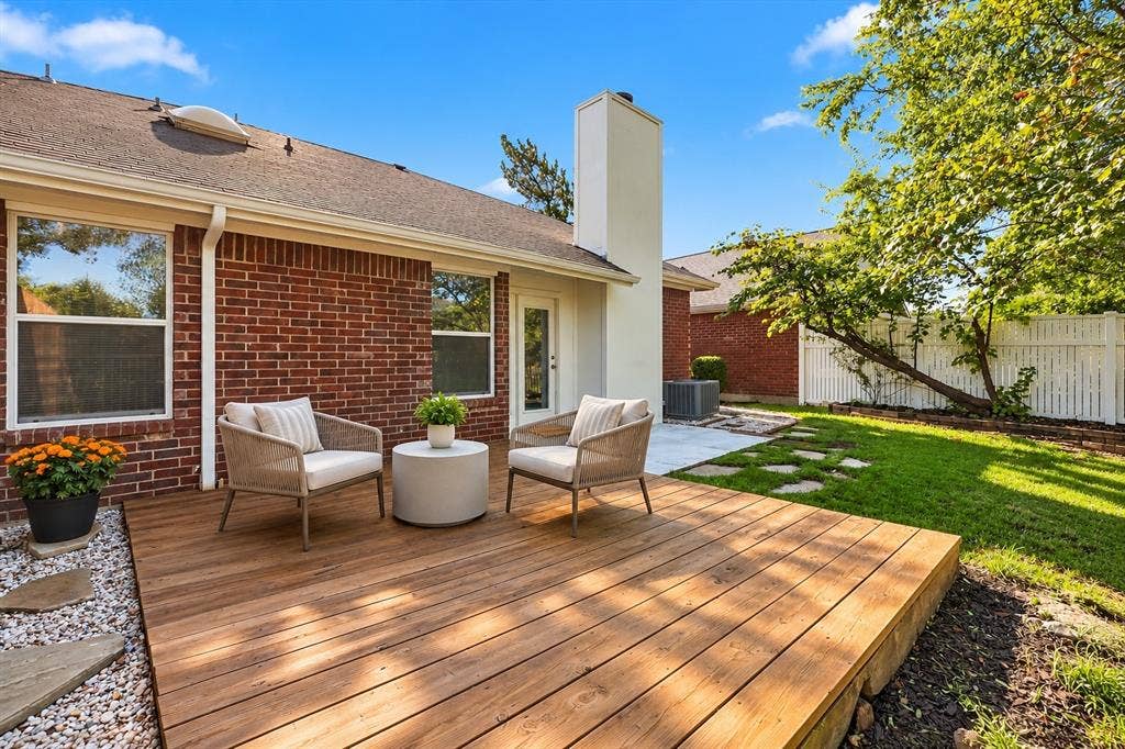 6821 Douglas Creek, Plano, TX 75023 Exterior featuring a red brick facade, wood-finish decking, white chimney stack, stone paver accents, and a fenced backyard