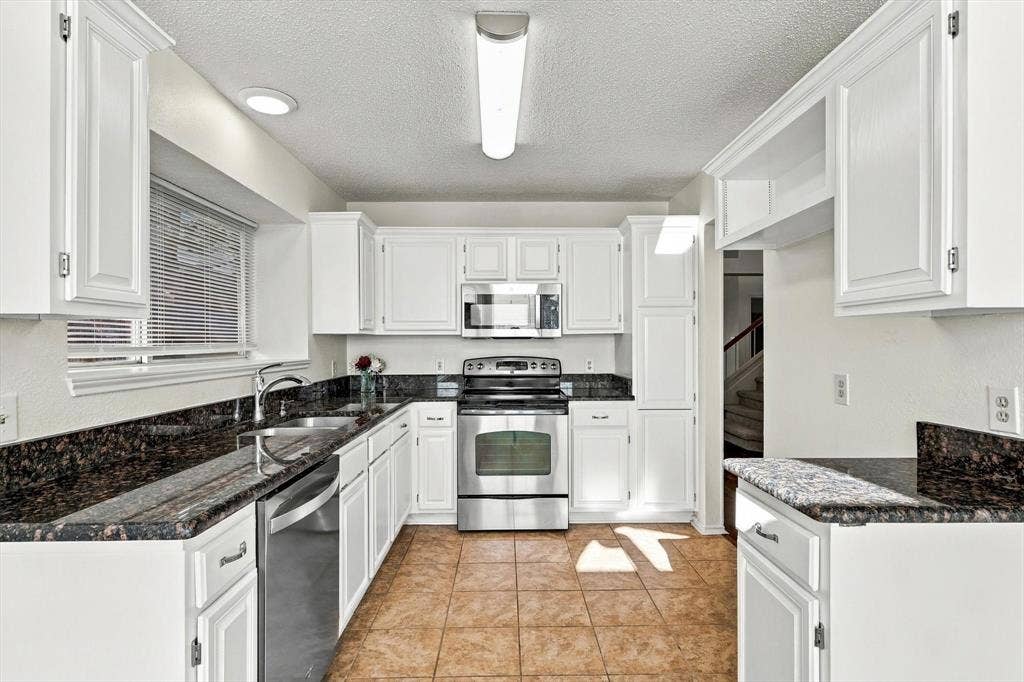 6821 Douglas Creek, Plano, TX 75023 Kitchen featuring white shaker-style cabinetry, stone countertops, tile flooring, and stainless steel appliances including an over-the-range microwave