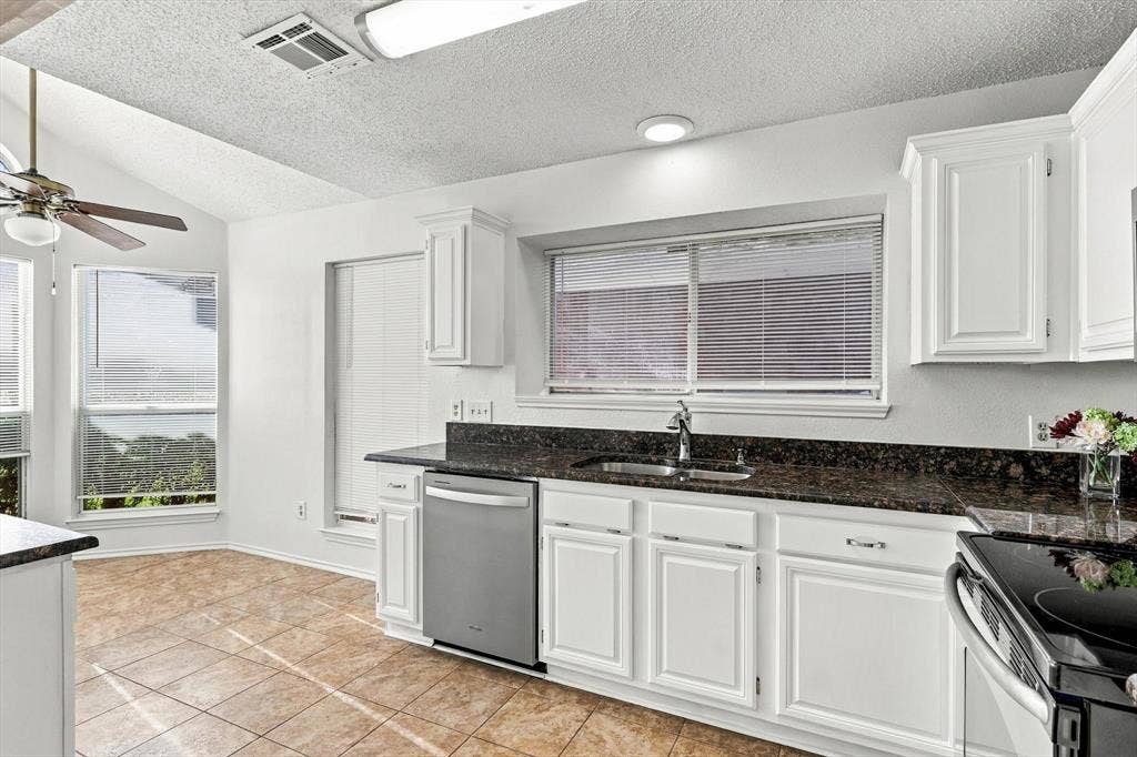 6821 Douglas Creek, Plano, TX 75023 Kitchen featuring white shaker-style cabinetry, stone countertops, stainless steel dishwasher, tile flooring, and vaulted ceilings