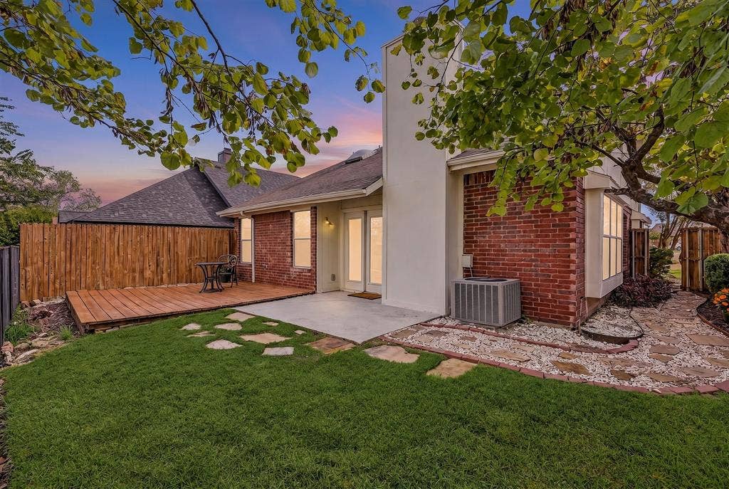 6821 Douglas Creek, Plano, TX 75023 Exterior featuring brick masonry, a wood deck, concrete patio, natural stone hardscaping, and wood fencing