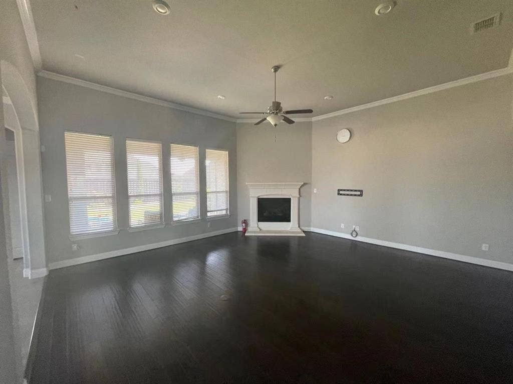 15112 Morning Star Lane, Frisco, TX 75035 Living area featuring wood-finish flooring, a corner fireplace with a decorative mantel, crown molding, a central ceiling fan, and four oversized windows with horizontal blinds