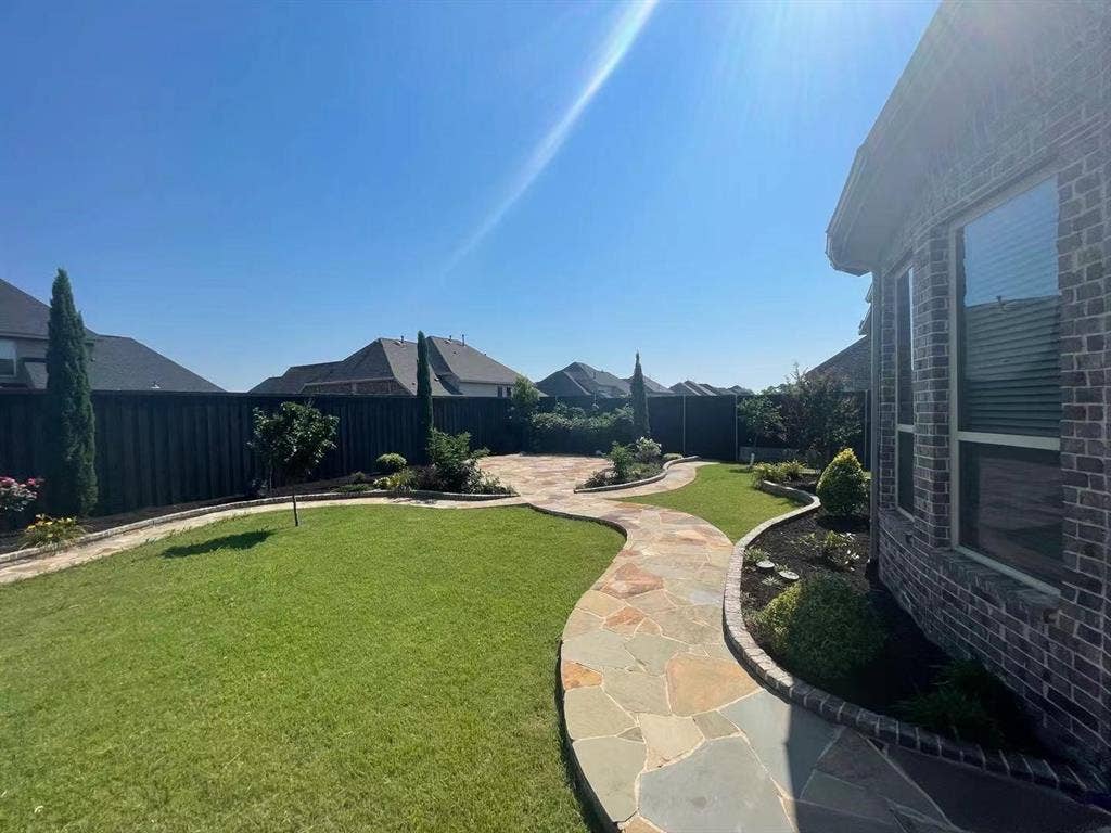 15112 Morning Star Lane, Frisco, TX 75035 Backyard featuring a flagstone patio, winding flagstone walkway, manicured lawn, established landscaping, and perimeter privacy fencing