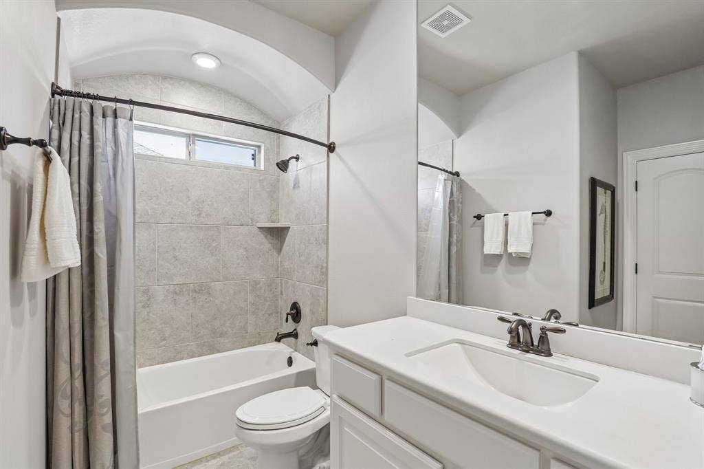 676 Princeton Way, Rockwall, TX 75087 Bathroom featuring a tub-shower combination with floor-to-ceiling tile surround, arched ceiling, white cabinetry with a solid-surface countertop, and oil-rubbed bronze fixtures
