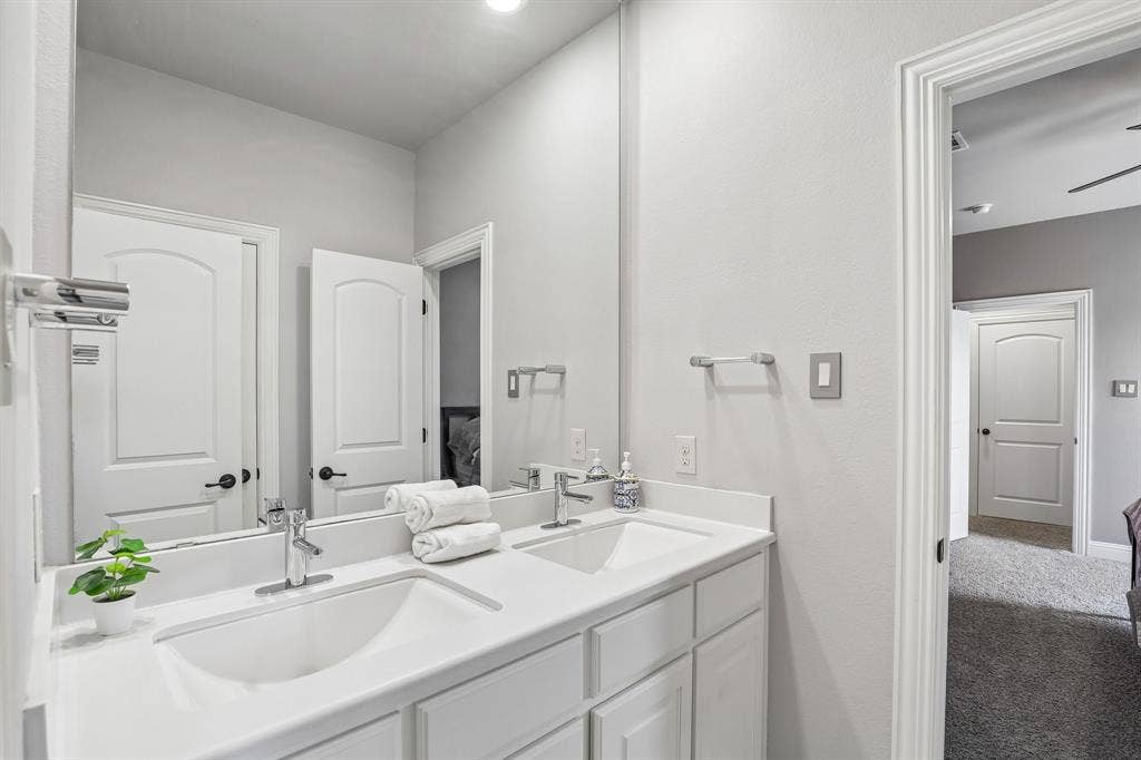 676 Princeton Way, Rockwall, TX 75087 Dual-sink vanity with a solid-surface countertop, full-width wall mirror, chrome fixtures, and white shaker-style cabinetry