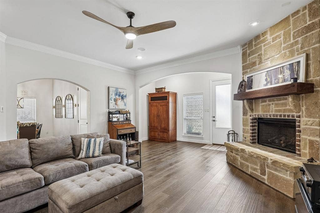 676 Princeton Way, Rockwall, TX 75087 Living area featuring floor-to-ceiling stone masonry fireplace with wooden mantel, wood-finish flooring, vaulted ceiling with integrated blade-style ceiling fan, and arched architectural entryways