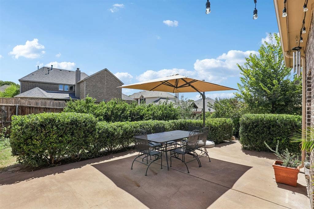 676 Princeton Way, Rockwall, TX 75087 Concrete patio featuring brick exterior wall, mature privacy hedging, and overhead string lighting