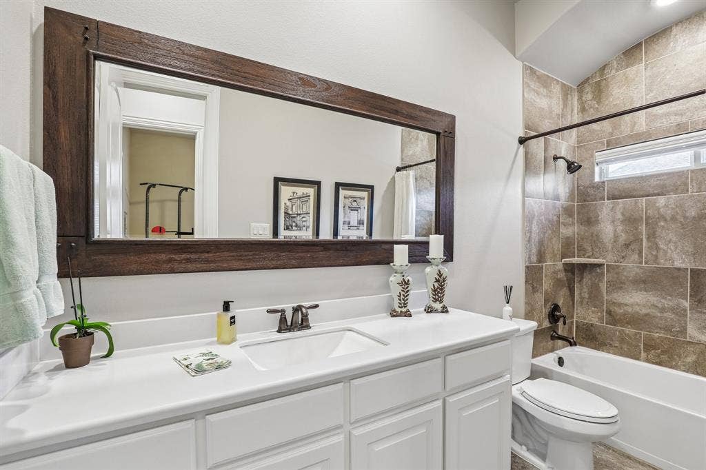 676 Princeton Way, Rockwall, TX 75087 Second downstairs bathroom featuring a white vanity with an integrated sink, a large mirror with a wood-finish frame, oil-rubbed bronze plumbing fixtures, and tile tub surround