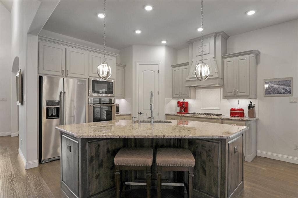 676 Princeton Way, Rockwall, TX 75087 Chef's kitchen featuring light-toned cabinetry, stone-surfaced center island, integrated stainless steel appliances, decorative pendant lighting, and wood-finish flooring