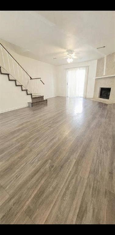 Wood-finish flooring, fireplace with stone surround, staircase with metal railing, and ceiling-mounted lighting